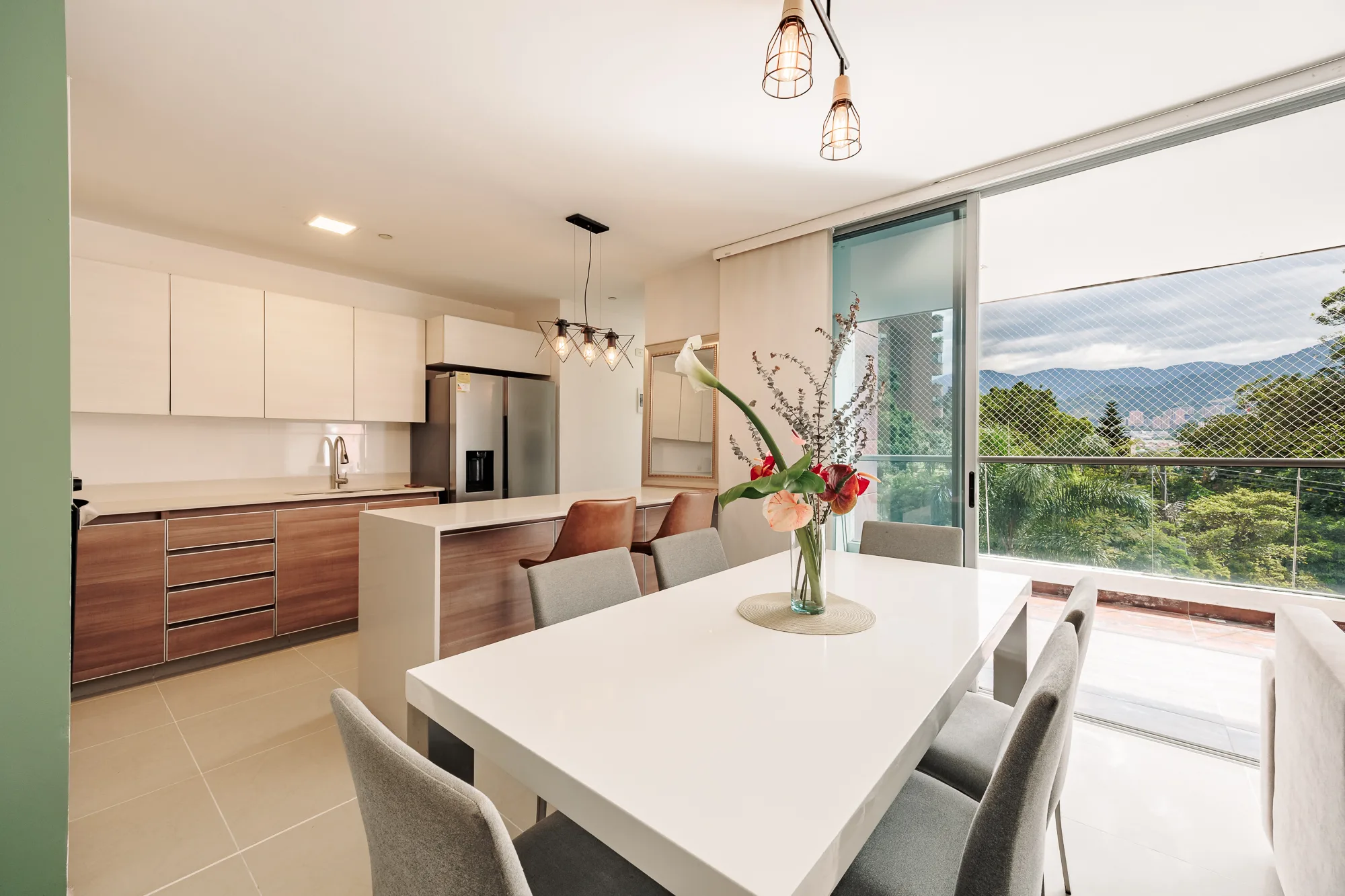 Dining table for six with the island kitchen and a mountain-view window behind at Balcón Verde