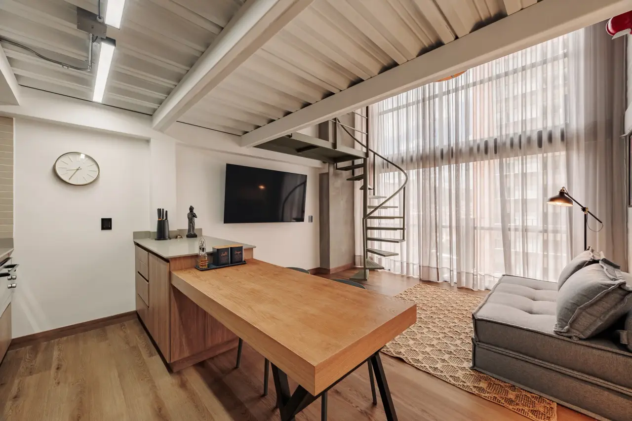 Downtown Loft — the open lower floor: dining table, kitchen counter and the spiral stair up to the mezzanine, Centro, Medellín