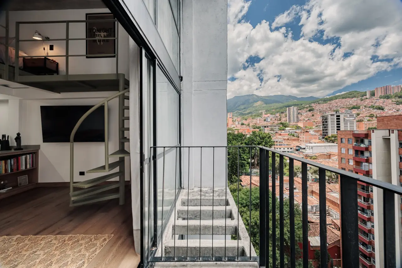 The private balcony at Downtown Loft, with the spiral stair and central Medellín beyond the glass