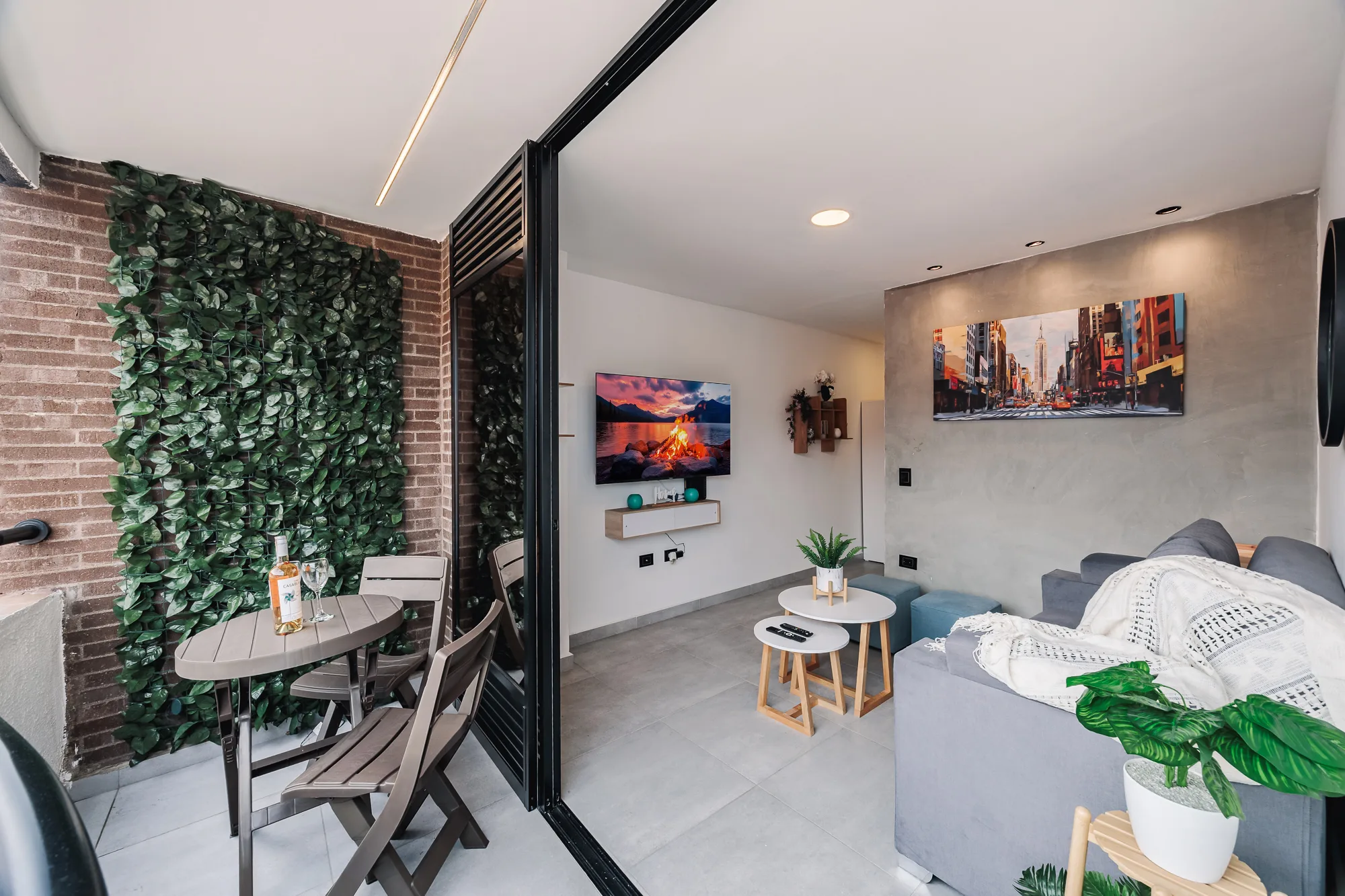 Itagüí Jacuzzi Suite — the living room seen from the balcony: a leafy green wall, a table for two and the TV wall