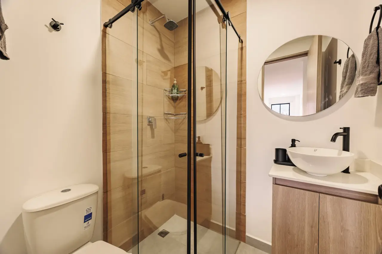 Bathroom with a glass shower, a round mirror and a vessel sink