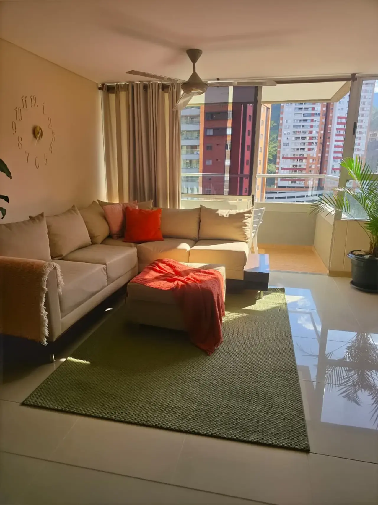 Living room at Sabaneta Parkside with a sectional sofa, a red throw and the city through the windows